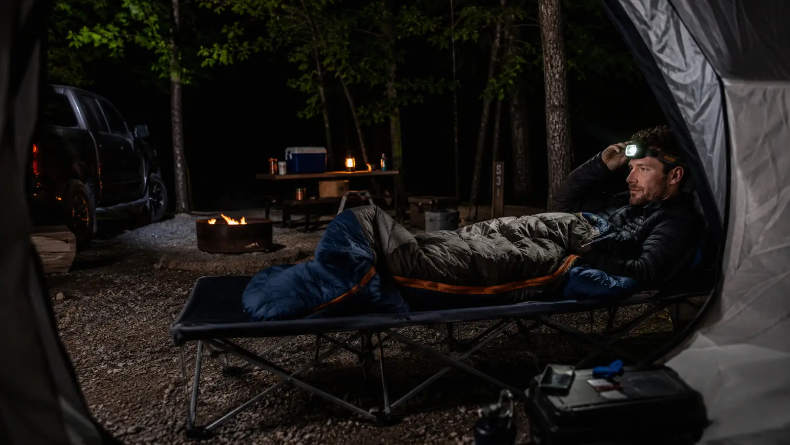 ARAER camping cot set up inside a tent at night with a headlamp resting on the frame
