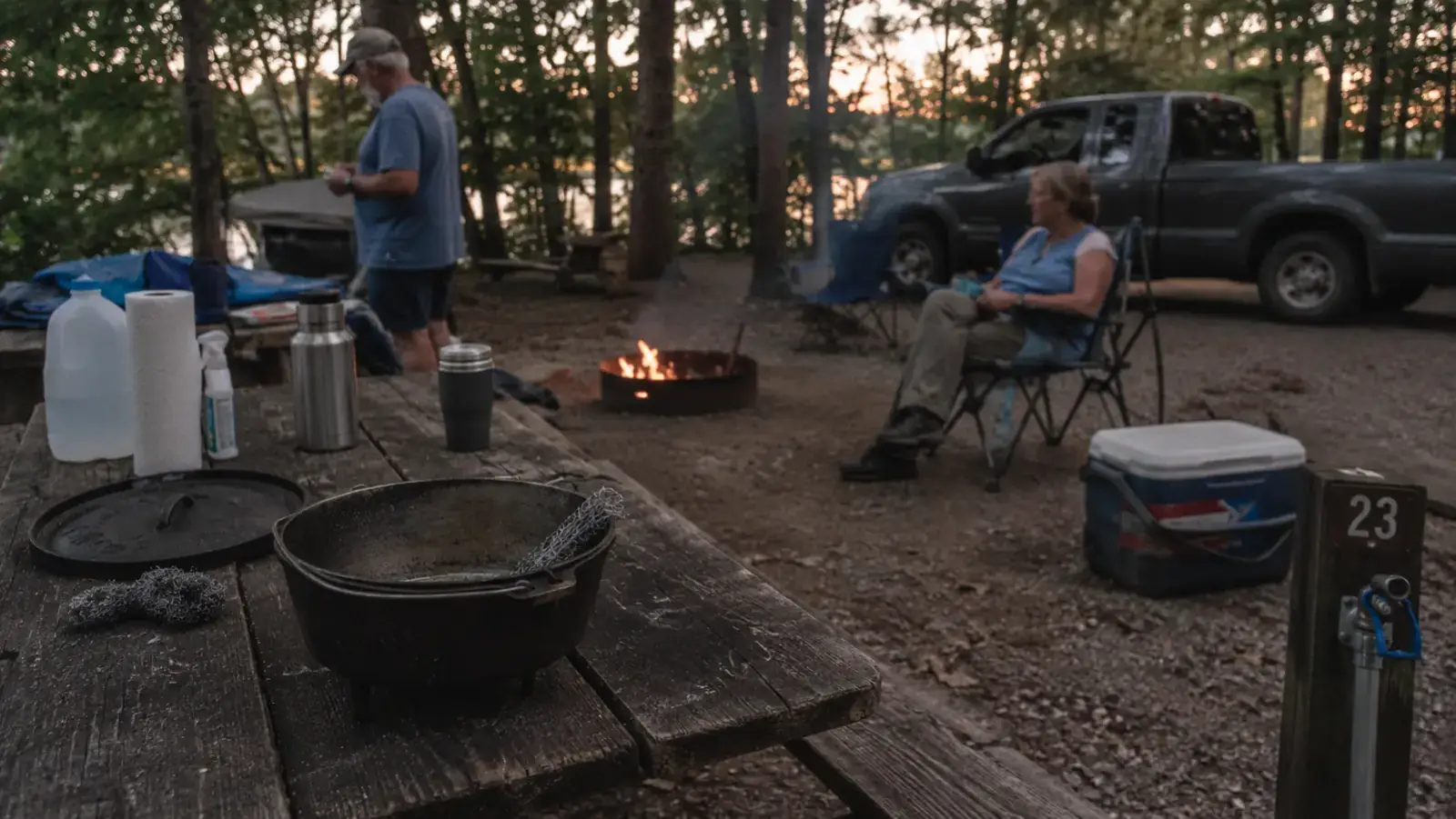 Cast iron camp dutch oven sitting half cleaned on a picnic table near a campground water spigot